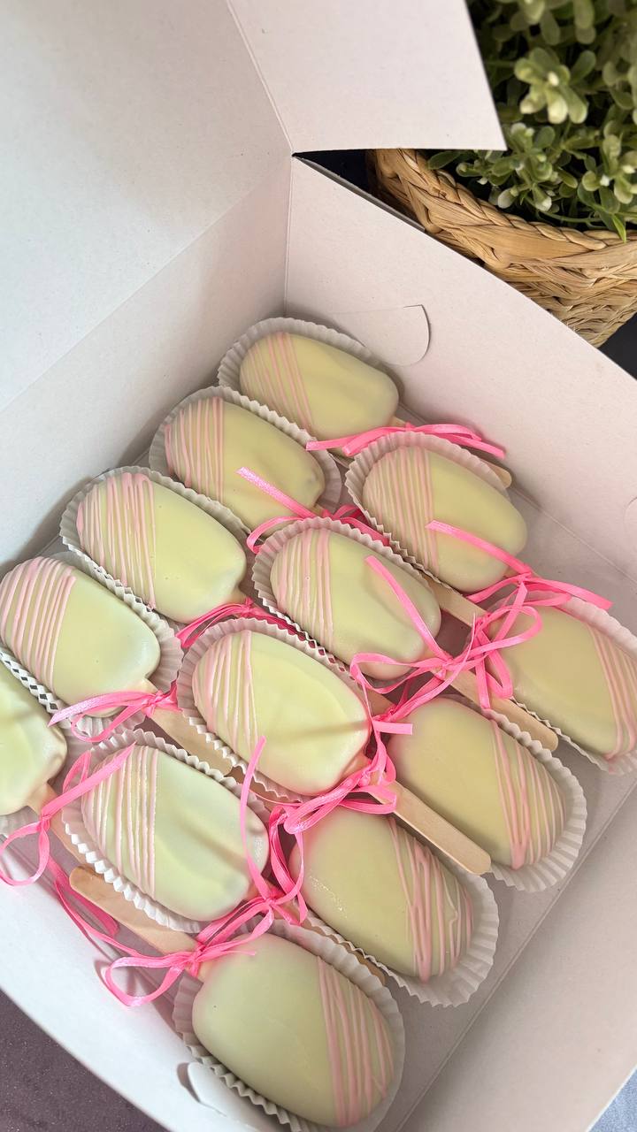 White chocolate cakesicles with pink drizzle and ribbons in a gift box